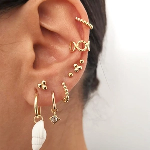7-piece gold earring set with evil eye stars and shells on model ear closeup