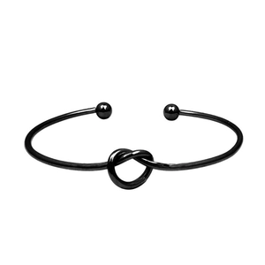 Macro shot of minimalist black knot bangle featuring a polished open-ended geometric design