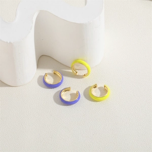 Macro detail of yellow and purple enamel C-shape ear cuffs on a white textured background