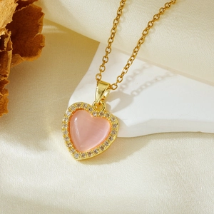 Detail of a gold heart necklace with pink opal stone and zircon edge on a white stone