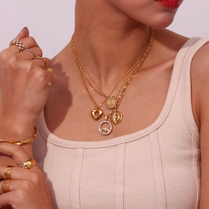 Close-up of layered 18K gold-plated necklaces and rings with heart and eye charms