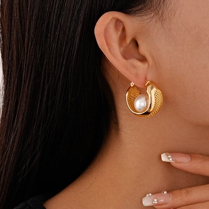 Detail of gold hollow mesh hoop earring with a large pearl inlay on model ear