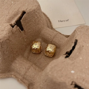 Macro detail of gold square hoop earrings with star engravings and small white crystals