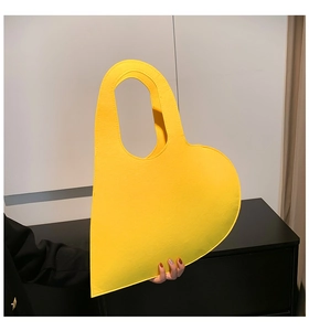 Detail of a bright yellow heart-shaped felt handbag with a modern cutout handle design