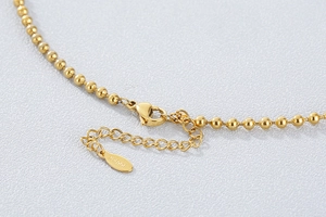 Macro detail of golden bead chain necklace with lobster clasp and engraved S.STEEL tag