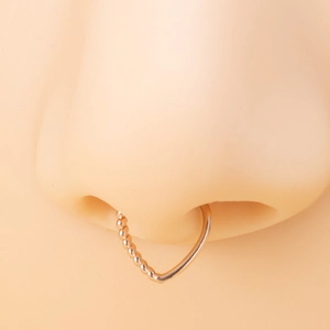 Macro detail of V-shaped rose gold nose ring with beaded texture and smooth finish