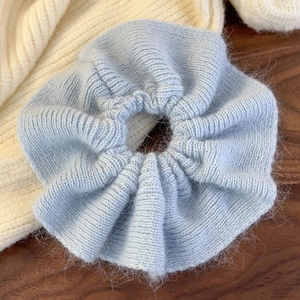 Close-up of light blue knitted scrunchie with soft mohair texture on wooden surface