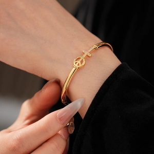 Detail of gold plated peace sign and diamond cross charm on an open cuff bracelet