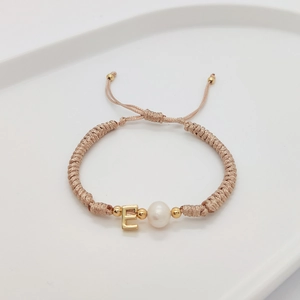 Detailed shot of handmade woven bracelet with freshwater pearl and golden letter E charm
