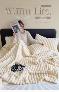 Close-up of beige faux rabbit fur blanket with ribbed texture on a cozy bed