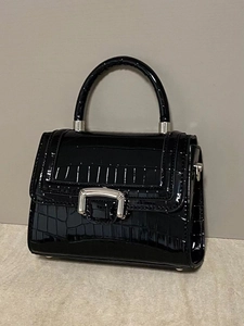 Macro detail of glossy black crocodile-patterned leather and silver hardware accents