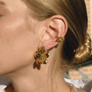 Nahaufnahme von goldenen Blumenohrringen und passender Ohrmanschette am Model