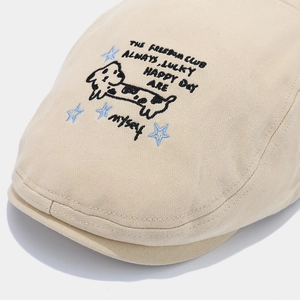 Detailed view of beige cotton flat cap featuring embroidered cartoon dog and text