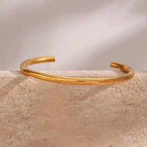 Polished 18K gold-plated minimalist bangle displayed on a natural porous stone base