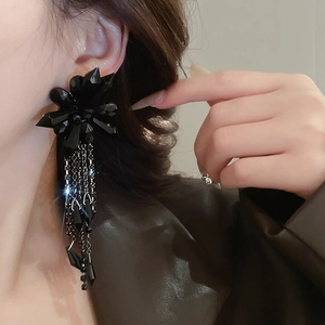 Close-up of black flower crystal earrings with long metallic fringe tassels on a model