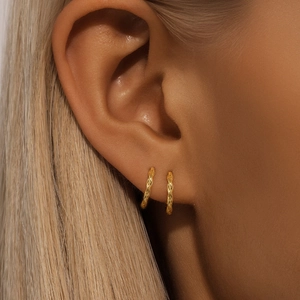 Close-up of golden rope-textured hoop earring showing intricate spiral details on ear