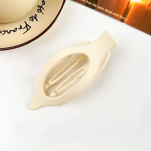 Macro shot of beige oval matte claw clip on a white desk with lifestyle props