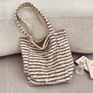Detail of plush brown striped tote bag with metal logo on a cozy lambskin pillow