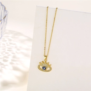 Detailed close-up of golden crown pendant with evil eye and zircons on a white display