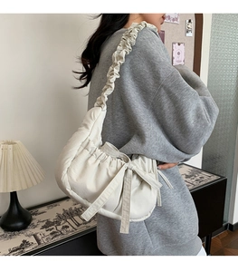 Detail of a creamy white pleated shoulder bag with bow detail and wavy strap on a model