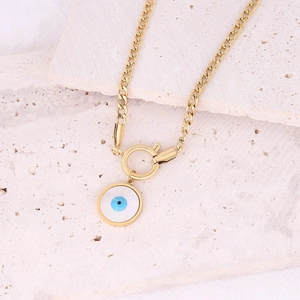 Detail of gold evil eye pendant with blue center on stainless steel chain over beige stone