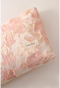 Detail of pink floral jacquard texture and woven brand label on the cosmetic bag