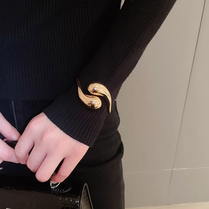 Detailed view of polished golden water-drop open cuff bracelet worn over black knit sleeve