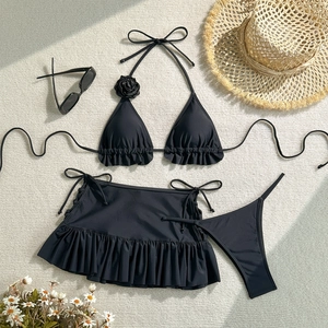 Flat lay of black three-piece bikini with 3D rose detail and ruffled skirt over beige fabric