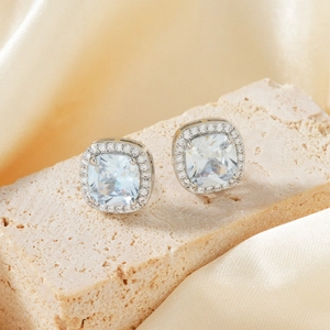 Macro shot of square cushion cut silver earrings with halo setting on champagne silk