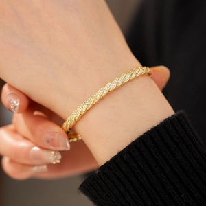 Macro detail of twisted gold-plated bracelet with pavé cubic zirconia on model's wrist