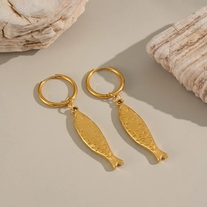 Close-up of gold fish pendant earrings with scale texture on natural stone background
