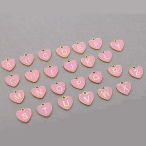 Flat lay of 26 heart-shaped pink enamel letter charms with gold metallic edges