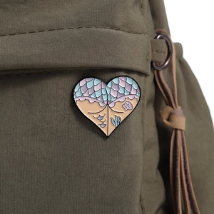 Detail of a heart-shaped enamel brooch with mermaid patterns on green canvas bag
