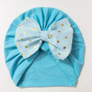 Detail of baby turban hat in light blue with gold polka dot bow on knit fabric