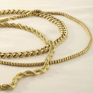 Detailed macro shot of 18K gold plated rope, curb, and bead chains on silk fabric
