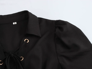 Detail of black dress featuring puff sleeves and lace-up neck with gold metal eyelets