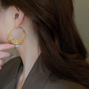 Close-up of gold-plated twisted hoop earrings on a model showing relief textures