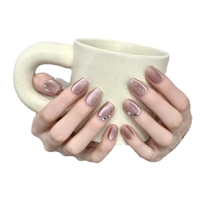 Short mauve pink cat eye press-on nails with rhinestone accents on hands holding a cup