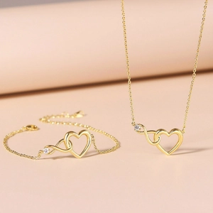 Gold-tone necklace and bracelet set featuring hollow heart and infinity symbol with gems