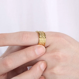 Macro view of a gold-plated stainless steel ring with intricate woven patterns worn on a finger
