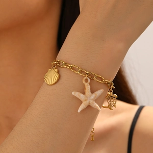 Detail of a gold stainless steel link bracelet featuring starfish and turtle charms on wrist
