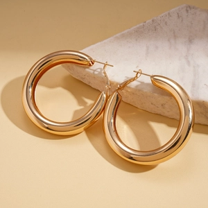 Macro detail of thick gold hoop earrings with high-polished mirror finish on marble