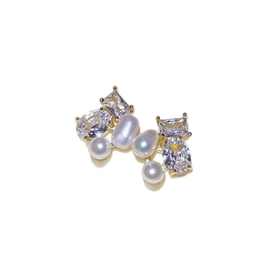 Elegant asymmetrical gold earrings with white pearls and zircons on white background