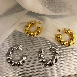 Dettaglio di orecchini a C intrecciati in oro e argento su uno sfondo elegante