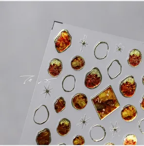 Macro detail of amber nail stickers with gold metallic edges and star patterns