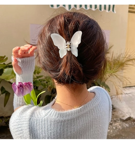 Detail view of a white butterfly hair claw clip securing a model's hairstyle outdoors