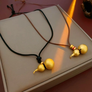 Detail view of gold gourd pendants on woven cords with elegant lighting in a gift box
