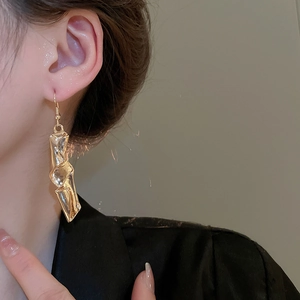 Close-up of golden irregular twisted metal long earrings worn by a model in a fashion setting