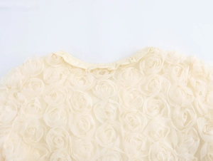 Close-up of cream cardigan featuring 3D floral rosettes and elegant round neckline