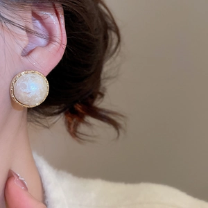 Detail of geometric pearl earring with gold-plated textured edge on female model